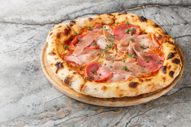 Charred meat pizza with prosciutto, salami, bacon and ham close-up on a wooden board. Horizontal