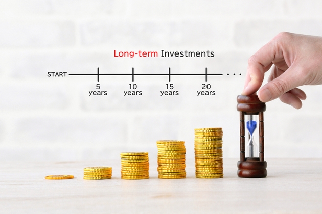 A person"s hand placing a pile of coins and an hourglass, image of long-term investment