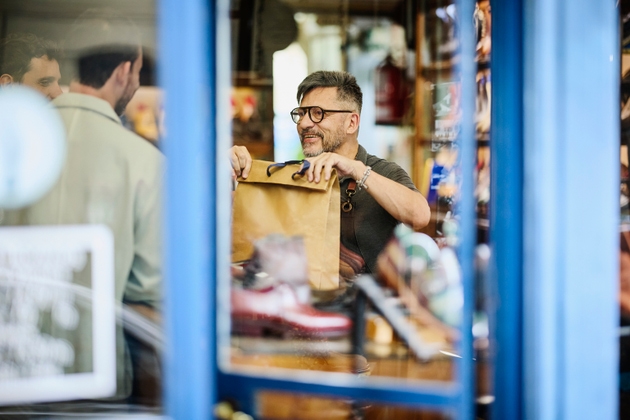 Medium shot male shop owner passing purchase in bag to male customer