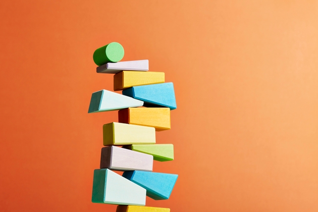 Unstable stack of irregular shaped geometric objects with a green cylinder on top