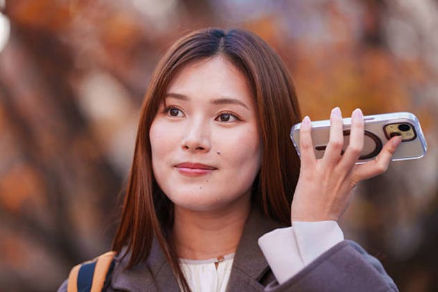 Young Japanese woman listening to voice message on smartphone outdoors