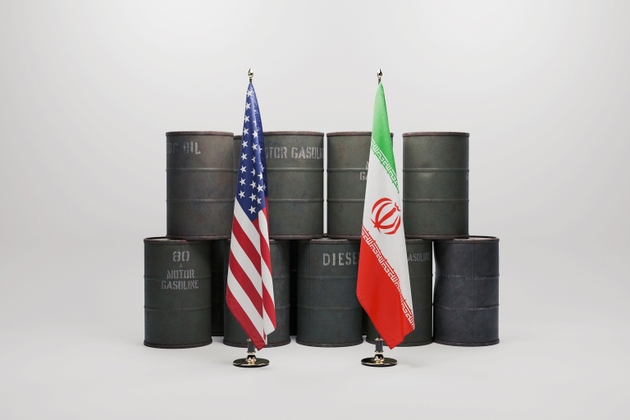 U.S. and Iranian flags stand before stacked oil barrels, symbolizing geopolitical tensions, energy security risks, and the potential closure of the Strait of Hormuz affecting global oil supply.