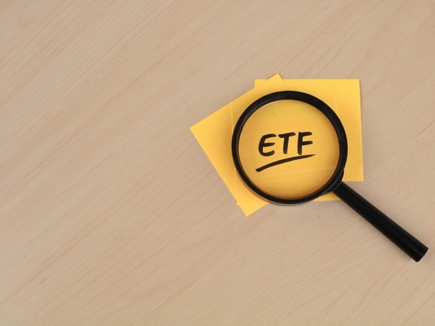 Magnifying glass over the acronym ETF written on a yellow paper on wooden desk