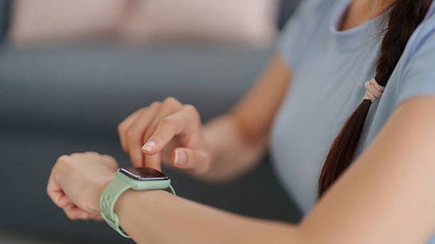 Asian adult woman tapping smartwatch screen monitoring fitness health activity digital tracking technology lifestyle casual indoor setting connectivity
