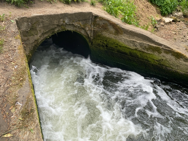 Stormwater rushing through concrete culvert pipe into open canal. Powerful water flow exiting round drainage tunnel into concrete channel. Foaming white rapids at outlet of sewer system