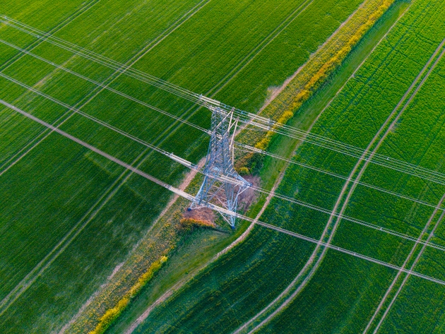 An overhead aerial/drone view of an electricity pylon in an green agricultural field in the UK