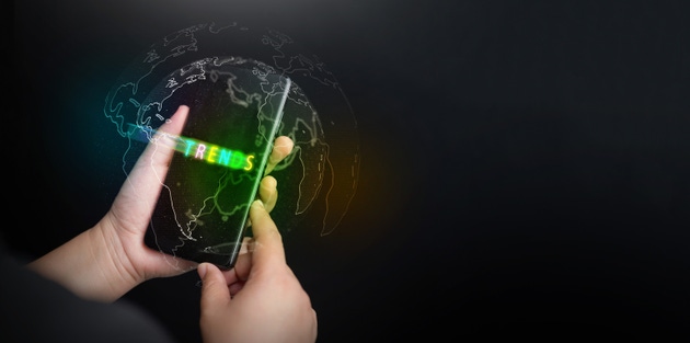 Business and technology trends concept. Hand holding smartphone with glowing neon text and a digital world map to represent global market analysis, mobile technology growth, and future data insights.