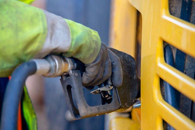 Worker fills machinery with fuel at a construction site during daylight hours in an urban setting