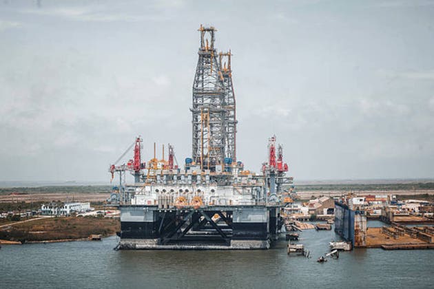 Massive offshore semisubmersible oil drilling rig docked at an industrial coastal shipyard facility