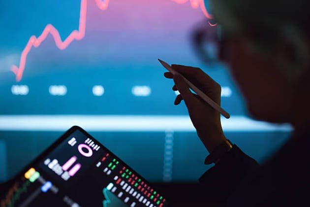 Investor Analyzing Stock Market Charts on Tablet and Screen With Stylus in Dim Office