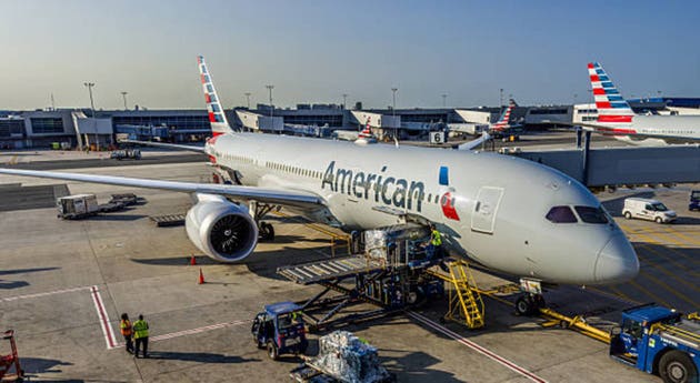 Ground crew workers load baggage and catering supplies onto an American Airlines passenger jet