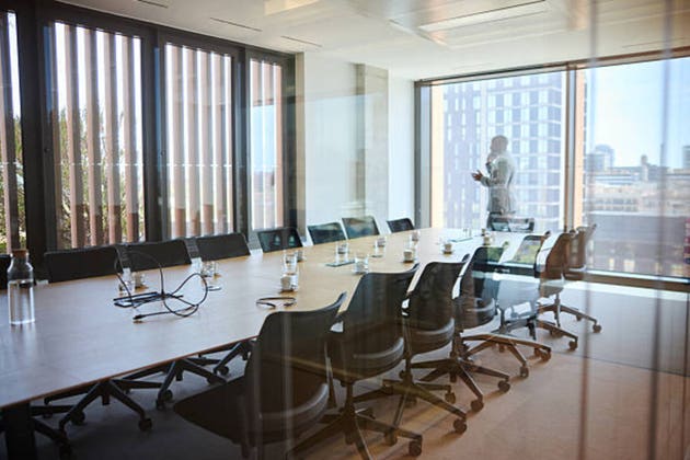 Prior to the senior management meeting, the businessman makes key phone calls to partners and clients. A man dressed in a suit is walking and talking on his phone in an entrepreneurship and corporate boardroom.