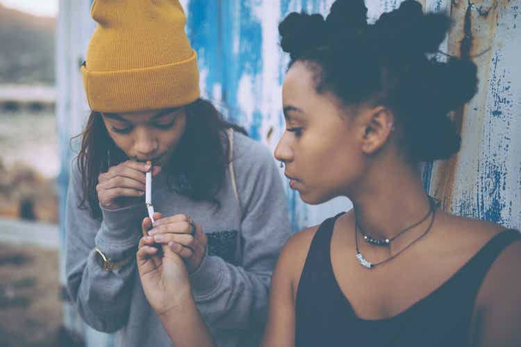 Afro teen lighting a cigarette for her grungy girl friend