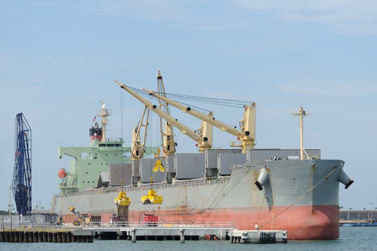 Cargo ship with cranes offloading dry bulk to dump trucks