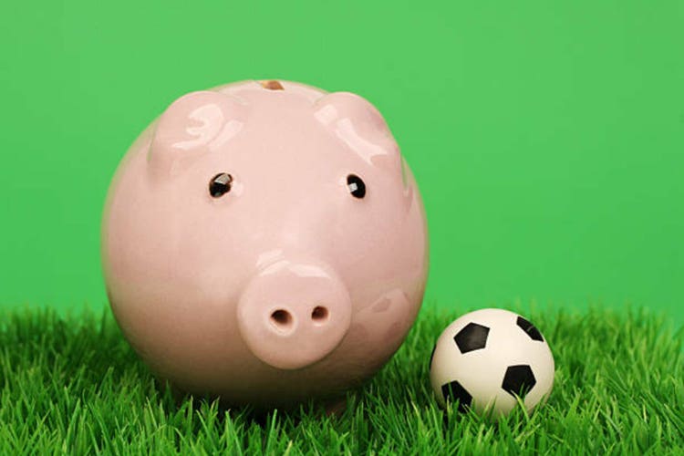 Pink piggy bank with soccer ball on a grass pitch