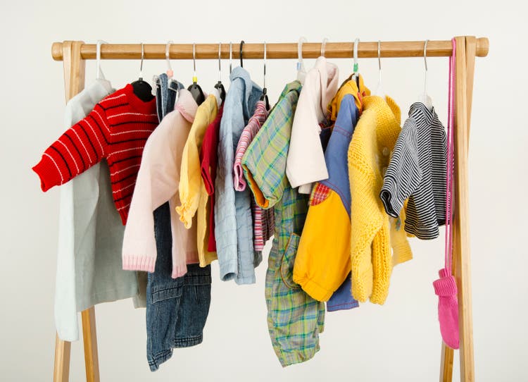 Dressing closet with baby clothes arranged on hangers.
