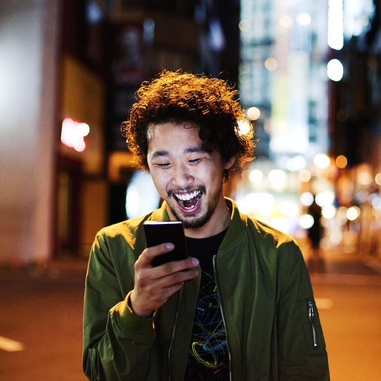 Joven japonés feliz con teléfono inteligente en la noche, Tokio.