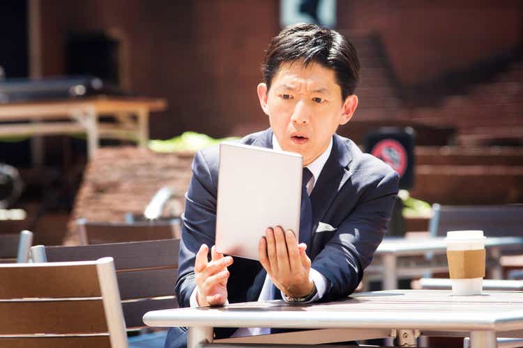 Japanese office worker reads shocking news on tablet outdoors