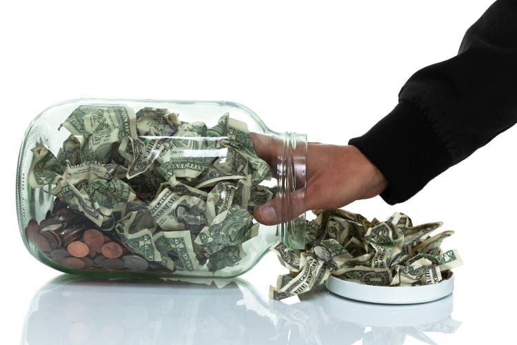 Hand in glass jar full of money tipped over