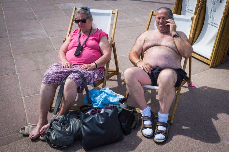 Senior sunbathers enjoying seaside sunshine on beach promenade deckchairs Dorset