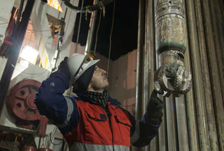 Engineer at rig site with drill bit looking upstairs