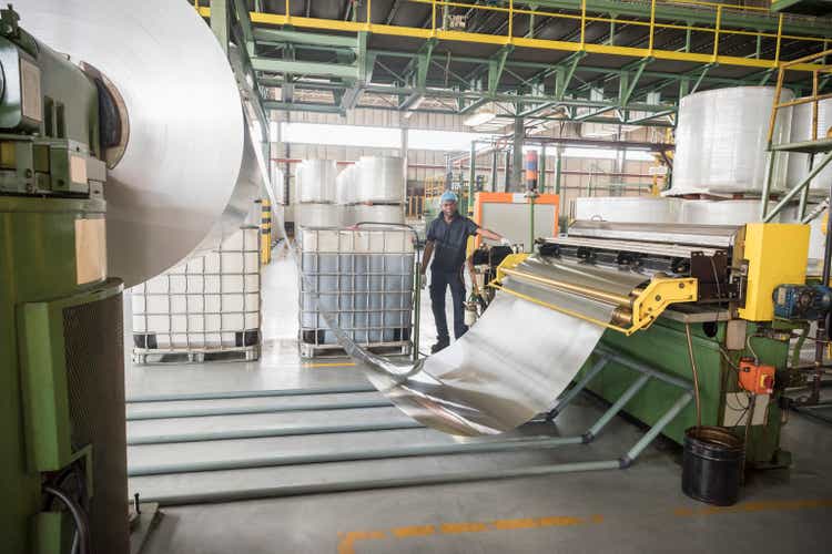 Man standing by large roll of aluminium in factory