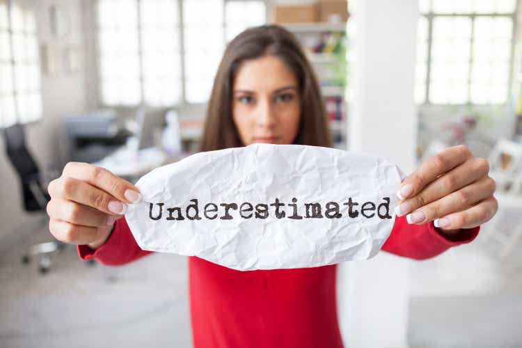 Young woman in the office holding sign "underestimated"