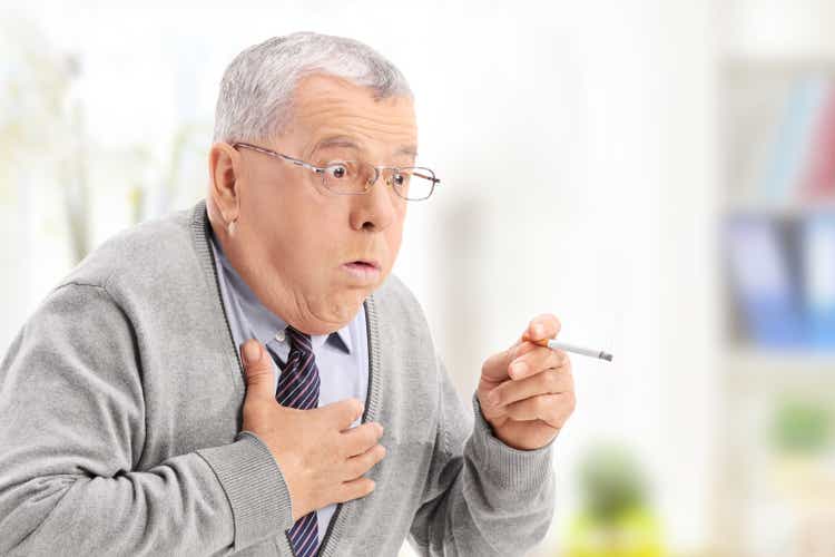 Senior man choking from the smoke of a cigarette