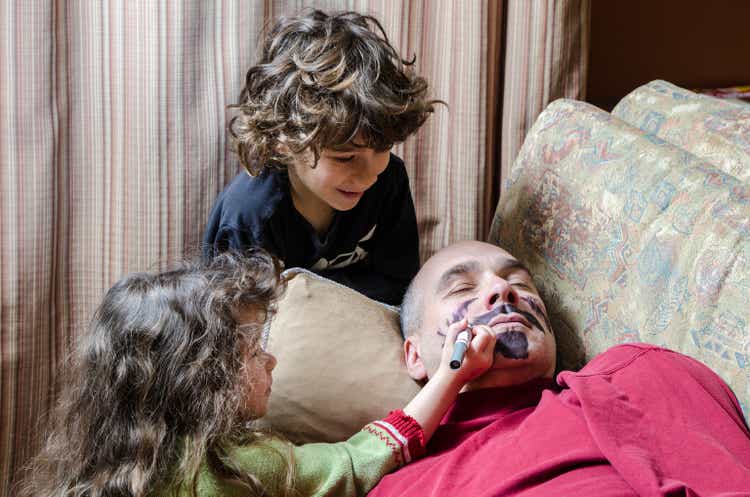 Children drawing a mustache on their father