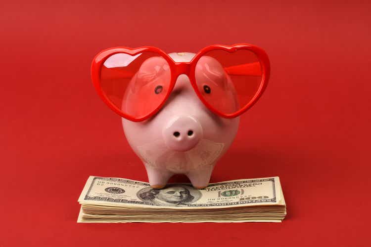 Piggy bank with heart sunglasses standing on stack of money