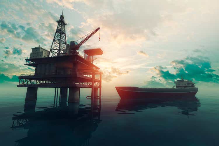 Sea oil rig with approaching tanker ship at sunset