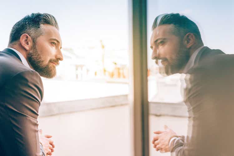 bearded business man reflecting himself in window glass
