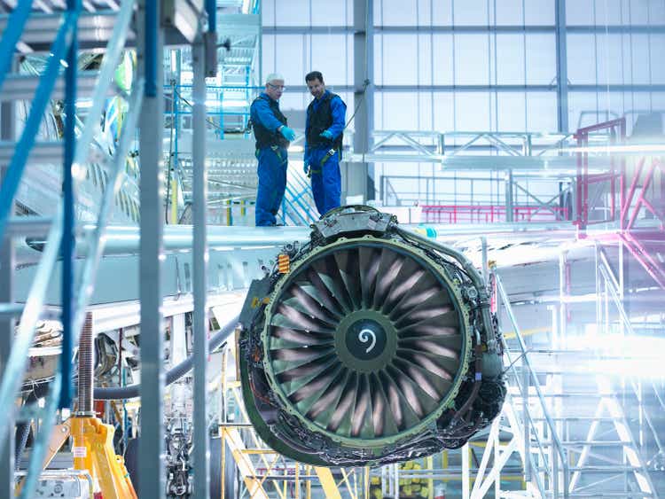 Aircraft engineers standing on wing with jet engine in aircraft maintenance factory