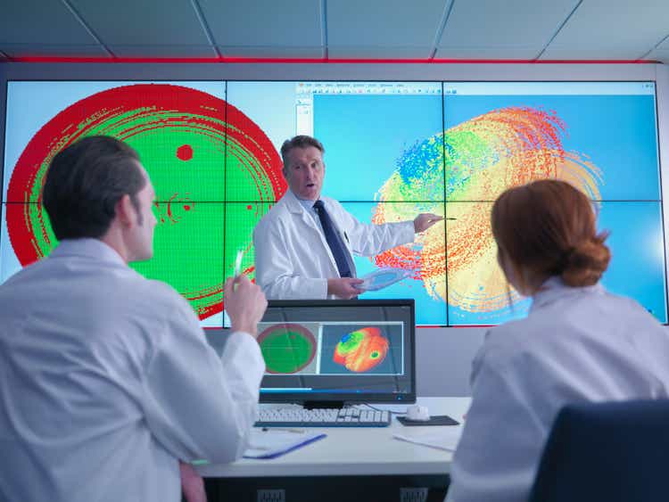 Scientists meeting in front of graphic display of silicon wafers on screen