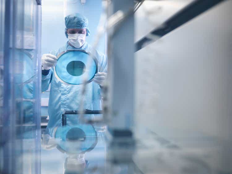 Electronics worker holding silicon wafer by cutting machine in clean room