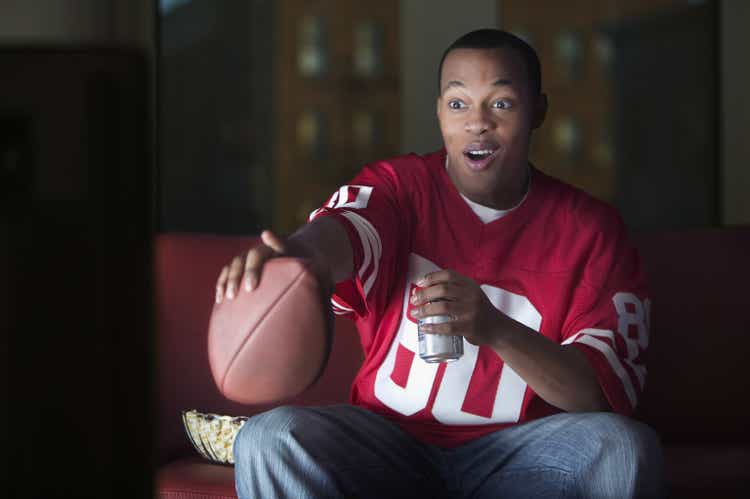 African American man watching television with football and beer