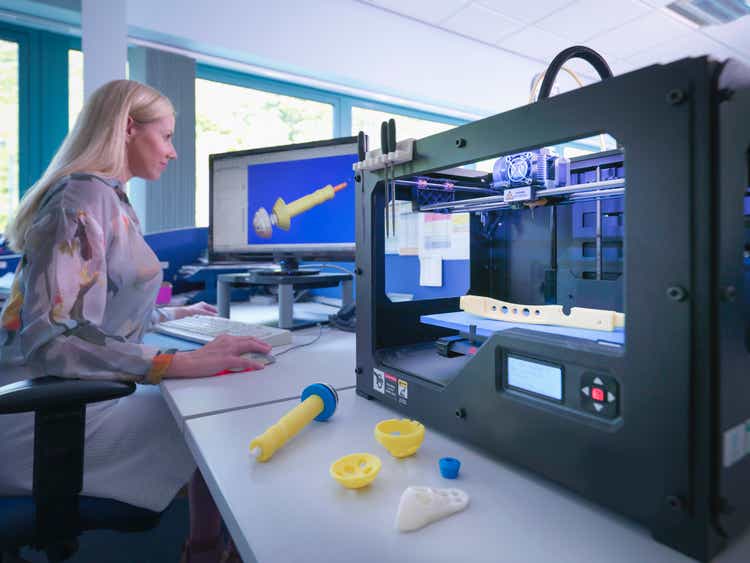 Medical product designer with 3D printing machine with CAD design on screen in orthopaedic factory
