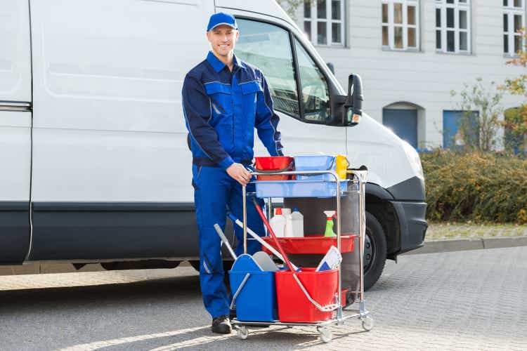 Happy janitor standing with cleaning equipment
