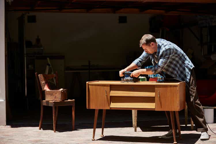 A man polishing furniture outside his house