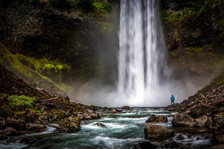 Man standing close to huge waterfall.
