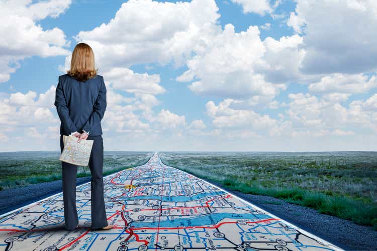 Businesswoman Stands On Long Road With Road Map Painted On It
