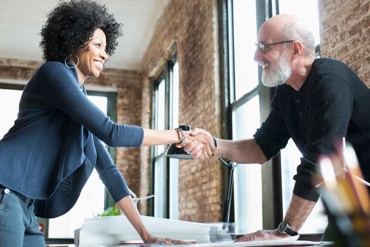 Business people handshaking over blueprints on desk