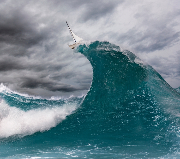 Sailboat balancing on top of enormous wave in ocean