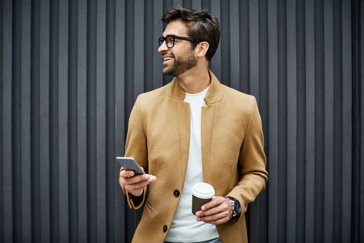 Smiling businessman with smart phone and cup