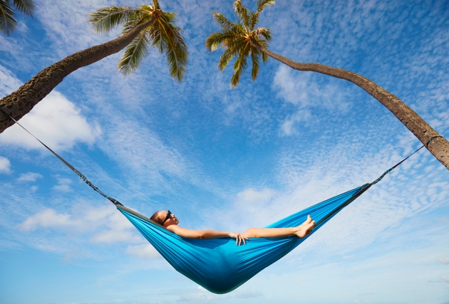 Pacific Islander woman laying in hammock between palm trees