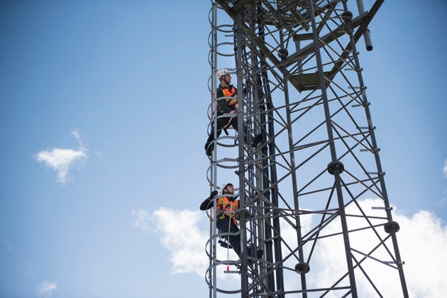 Engineers climbing transmission tower, low angle view
