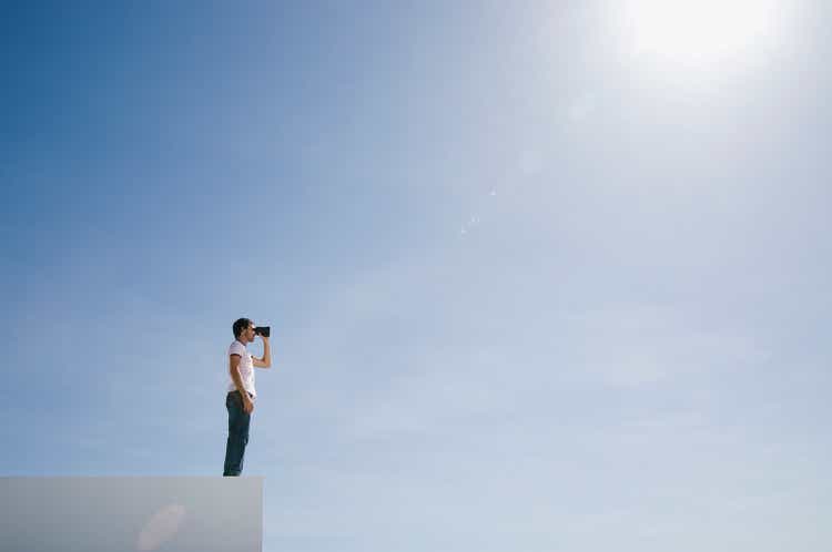 Man on pedestal with binoculars and blue sky outdoors