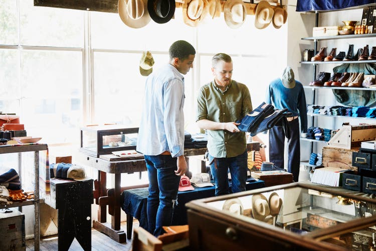 Shop owner explaining difference in denim jeans to customer in store