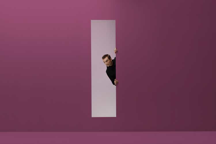 Man peeking threw rectangular opening in coloured room