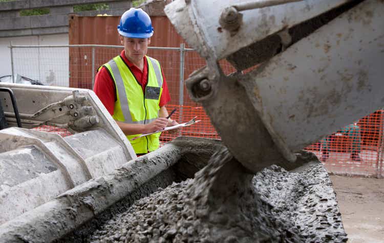 Construction workers watch concrete being poured from a truck